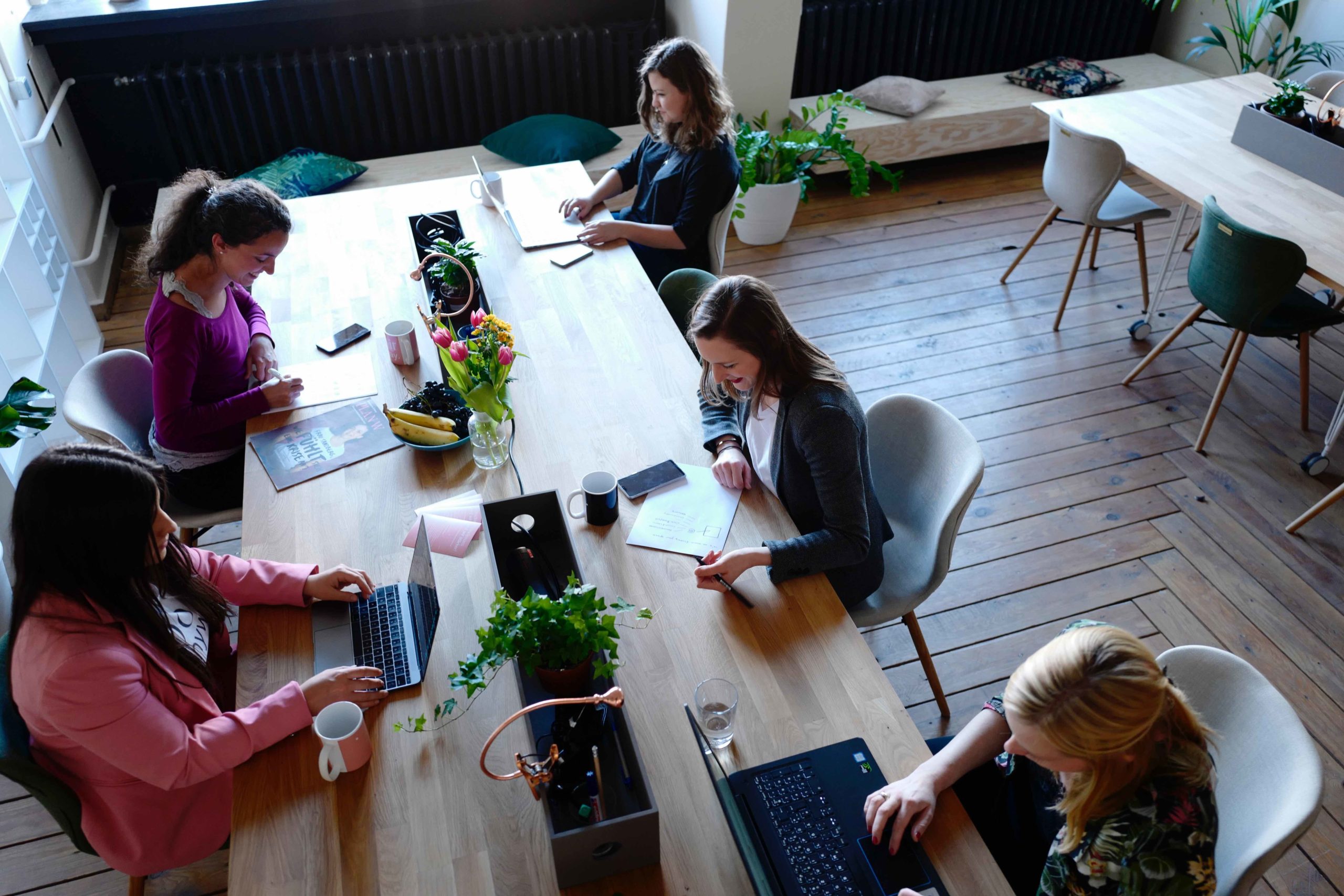 Overhead view of women working together at large table with laptops in bright modern office space