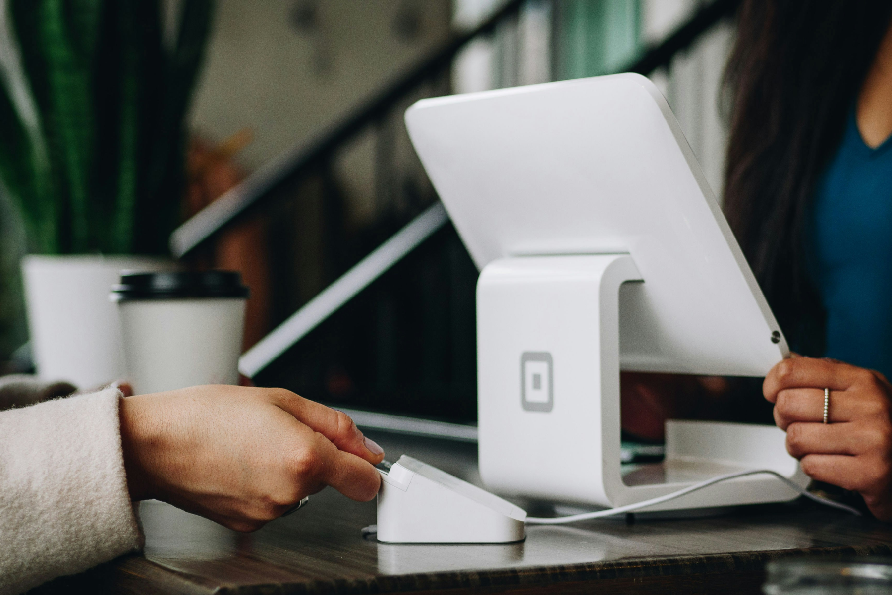 Hands using Square payment system with tablet and card reader on desk.