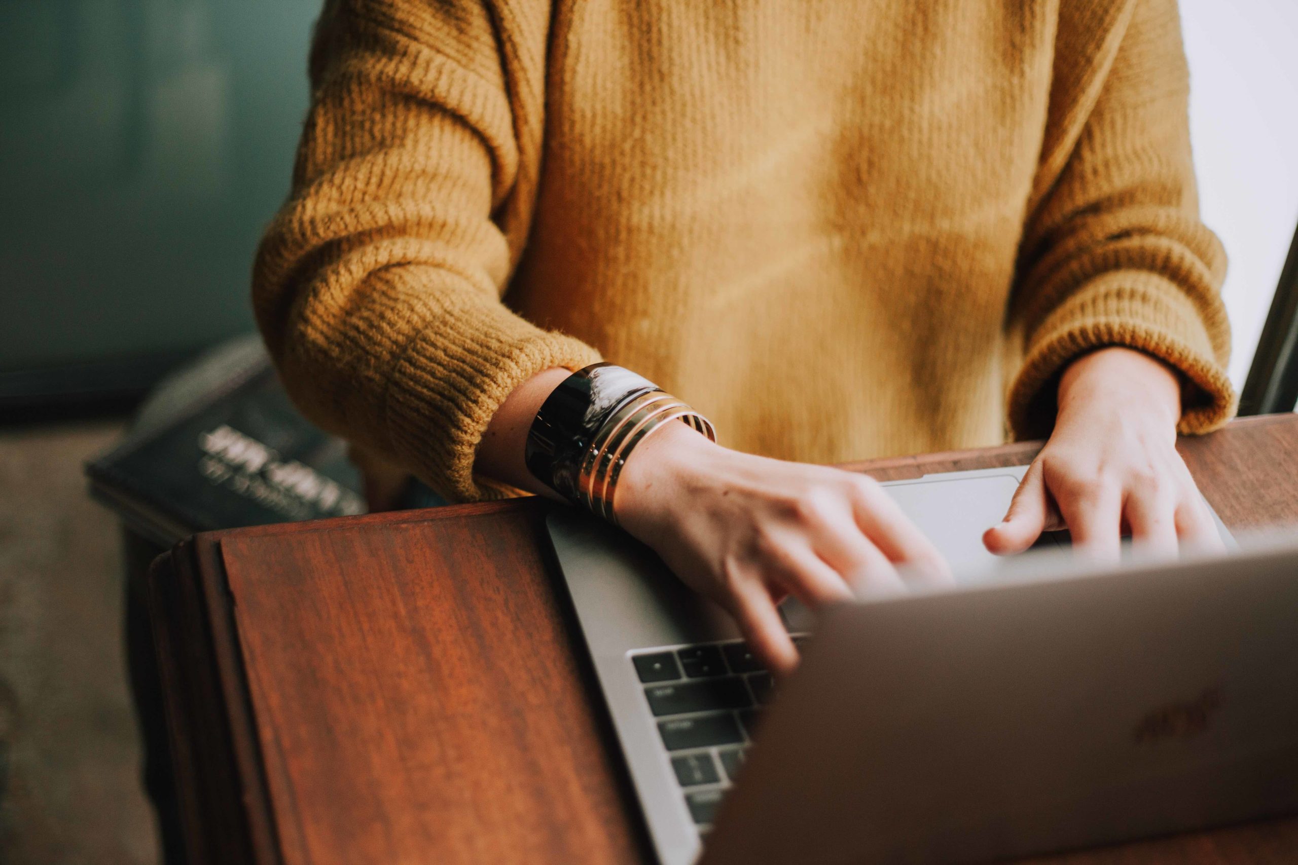 Person in tan sweater working on laptop, close-up of hands and bracelet