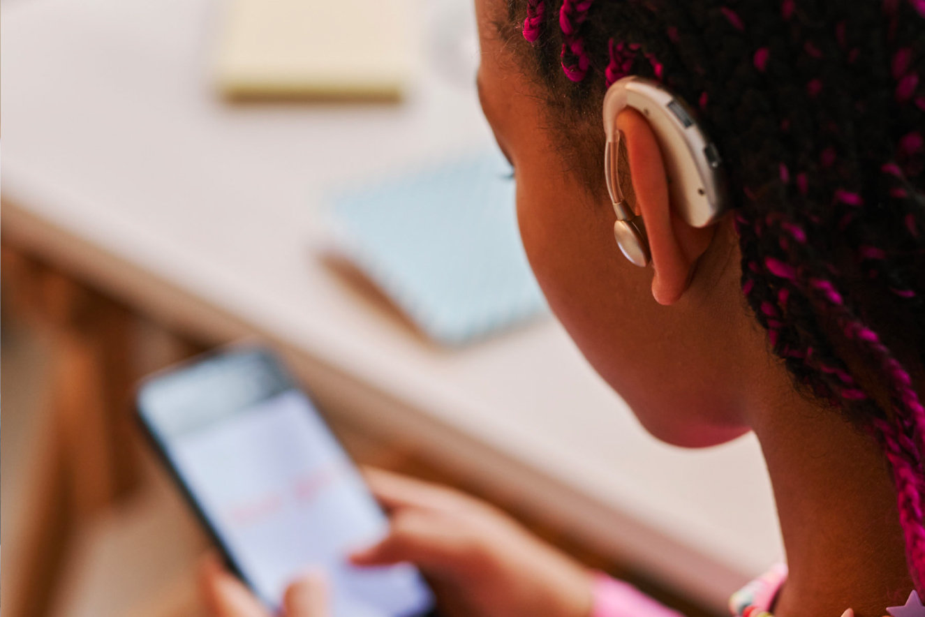 A teenager with a hearing aid using a smartphone