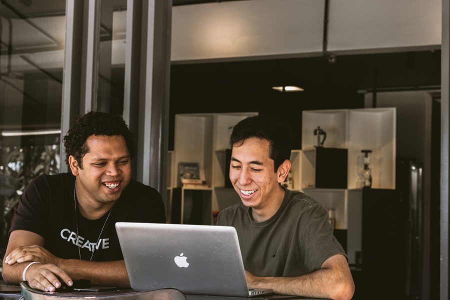 Two colleagues smiling while collaborating on a MacBook laptop in an office space