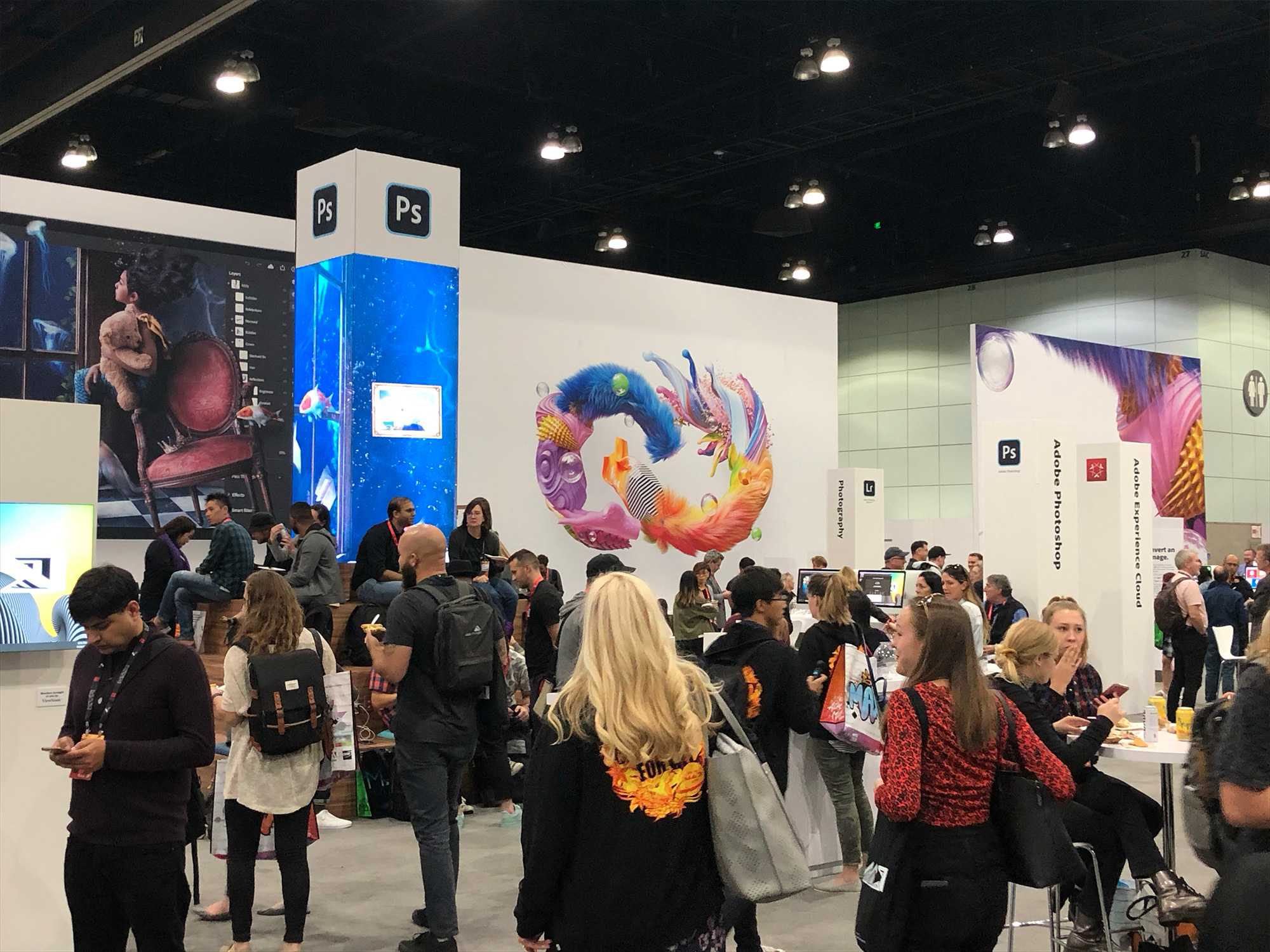 Adobe Photoshop booth at a convention with large PS logos, creative artwork displays, and crowd of attendees