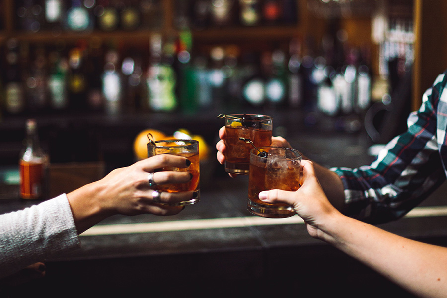 Friends toasting with cocktails at bar, focused on glasses clinking together